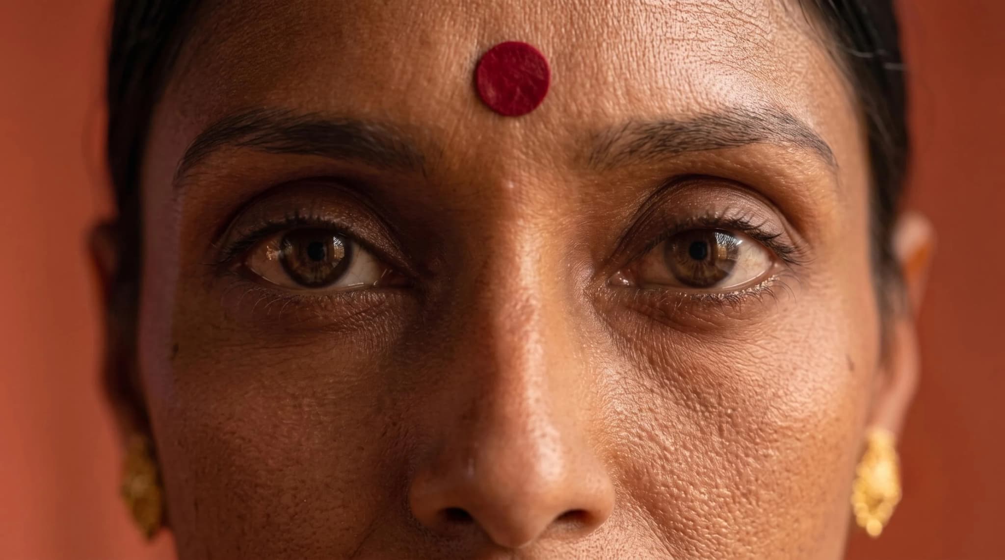 Close crop of the model's eyes and bindi against a terracotta wall