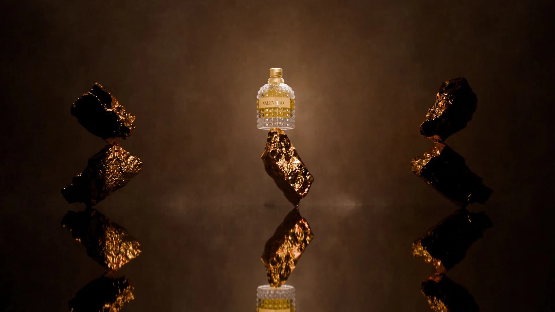 The perfume bottle centred between gold fragments on a dark reflective surface