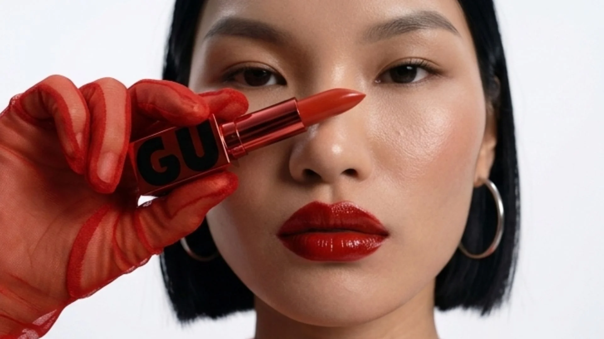 Model holding the GURU lipstick beside her face, her hand painted red